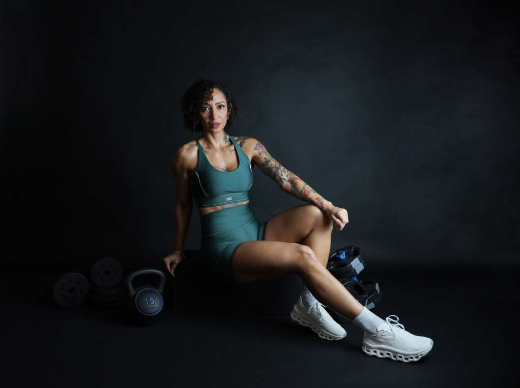 Flávia Ribeiro sentada ao lado de halteres e kettlebell
